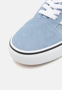 Blå mockaskor med vita snören, gummisula, svart kant och texturerad yta. Rundad tådesign, synlig sömnad på ovandelen.