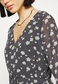 Vestido floral com um fundo escuro, apresentando pequenas flores brancas e azuis. Design em V e mangas transparentes, complementado por um colar metálico.