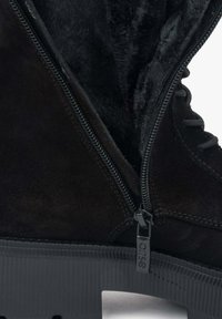 Czarny zamszowy botek na kostkę z grubą gumową podeszwą, wyposażony w boczny zamek błyskawiczny oraz miękką, fakturowaną podszewkę widoczną w środku.