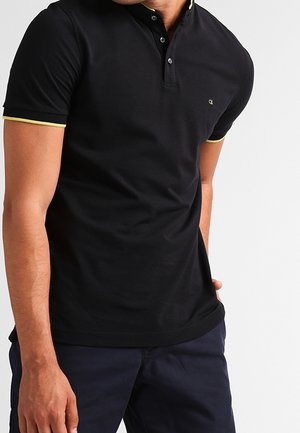Polo negro con un cierre de dos botones, ribete amarillo en el cuello y las mangas, y un pequeño logo en el pecho. Manga corta, diseño ajustado.