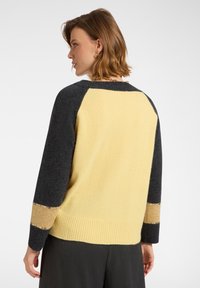 Sweter z dzianiny w kolorze żółtym, z ciemnoszarymi rękawami i ściągaczem u dołu. Udekorowany teksturowaną taśmą i ozdobnymi detalami.