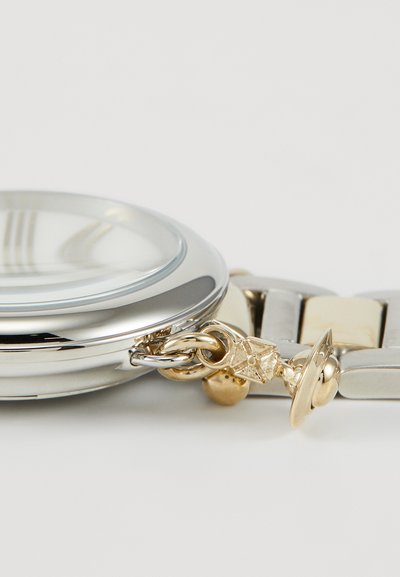 Ασημένιο και χρυσό ρολόι χεριού με στρογγυλό κάσα, λείο γυαλί, μπρασελέ από συνδέσμους και διακοσμητικά αξεσουάρ.