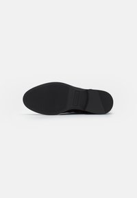 Sort sko sål med tekstureret grip mønster, let hæl og indgraveret mærke label i midtersektionen på hvid baggrund.