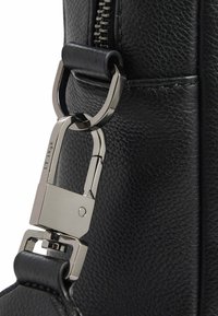 Nahaufnahme einer schwarzen Ledertasche mit einem silbernen Metallverschluss und -beschlägen, einer strukturierten Oberfläche und einem Reißverschlussdetail.