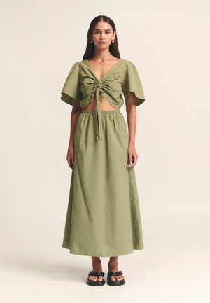 Světlý zelený dvoudílný outfit skládající se z nařaseného krátkého topu s krátkými rukávy a dlouhé maxi sukně s vysokým pasem. Hladká textura, jednoduchý design.