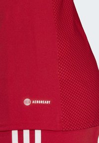Maglietta sportiva rossa con pannello laterale testurizzato, tessuto liscio, logo AeroReady in bianco e tre strisce bianche nella parte inferiore.