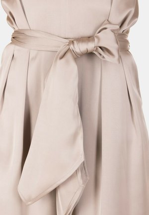 Cintura in tessuto beige annodata a fiocco intorno alla vita di un abito o cappotto plissettato.