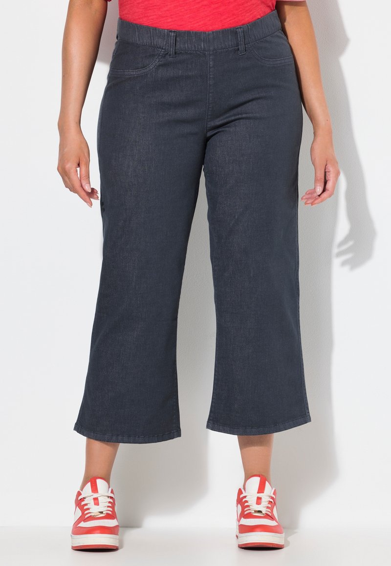 Pantalones de denim azul oscuro recortados con un corte relajado, que cuentan con una cinturilla elástica y dos bolsillos frontales. Combinados con zapatillas rojas y blancas.