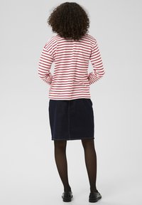 Punaste ja valgete triipudega pikkade varrukatega särk, mida on kombineeritud tumeda teksaseelikuga. Komplekt on sirge lõikega ja sellel on nähtavad õmblused.