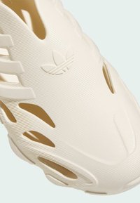 White slip-on shoe made of textured rubber. Features cut-outs for ventilation and three parallel stripes along the side.