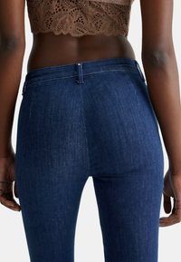 Jeans in denim blu scuro con un design aderente, caratterizzati da uno stile classico a cinque tasche e una texture liscia, con vista posteriore.