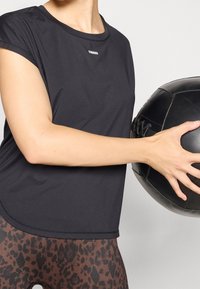 Sort atletisk T-shirt med korte ærmer, har en rundet kant og ordet "STRONGER" i hvid. Parret med brune leggings med leopardprint.