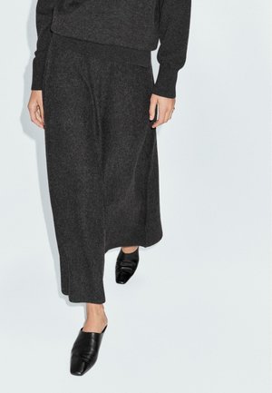 Jupe longue en laine gris foncé avec une coupe décontractée et une taille plate, associée à des mules en cuir noir à bout pointu.