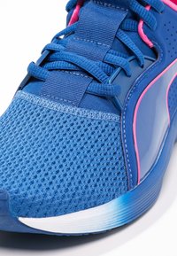 Blue athletic shoe with mesh upper, shiny accents, contrasting pink details, and a curved white sole with light blue gradient.
