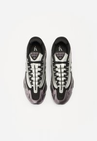 Scarpe sportive nere e argento con parte superiore in rete testurizzata, dettagli lucidi e punta arrotondata. Presentano lacci neri e branding ricamato.