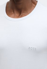 Svetlo modra bombažna majica s okrolim izrezom in subtilnim vezenim logotipom "BOSS" na prsih. Gladek tekstura z minimalističnim dizajnom.