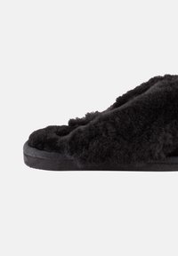 Zwarte met bont gevoerde slide-sandaal met een platte zwarte zool, voorzien van een textuur met echt fluffy bovenkant en een eenvoudig open teen ontwerp.