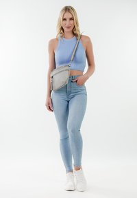 Borsa a tracolla grigia dal design elegante, con chiusura a zip. Il modello indossa un top a coste azzurro chiaro e jeans skinny azzurro chiaro con sneakers bianche.