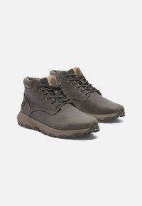 Botas de cuero marrón hasta el tobillo con detalles grises, que presentan ojales de metal, lengüeta texturizada y una suela de goma resistente para mayor tracción.