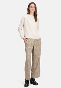 Jasno beżowa bluzka z długim rękawem, o okrągłym dekolcie i guzikach na ramionach, w połączeniu z brązowymi spodniami w kratę o szerokich nogawkach oraz czarnymi botkami za kostkę.