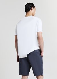T-shirt blanc à manches courtes avec un ourlet arrondi, associé à un short gris foncé texturé, doté de poches latérales et d'une coupe décontractée.