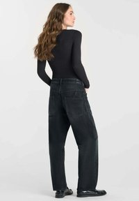 Top noir à manches longues associé à un jean en denim sombre à coupe ample. Le jean présente de grandes poches arrière et une taille haute.