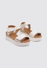 Sandalias de plataforma blancas con parte superior texturizada, correas ajustables y una plantilla marrón. Suela de cuña baja en un color claro contrastante.