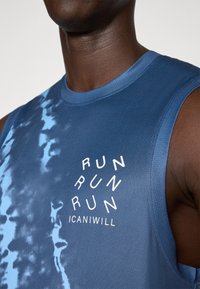 Débardeur de sport sans manches en bleu dégradé avec une finition texturée. Présente un graphique circulaire blanc avec les mots "COURIR" et "ICANIWILL".