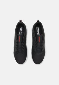 Črne atletske čevlje z teksturiranim mrežastim zgornjim delom, z vezalnim zapiranjem in blagovno znamko Reebok. Imajo belo gumo podplat in rdeče detajle.