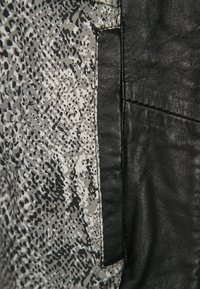 Rifiniture in pelle nera accanto a un tessuto con stampa animale grigia e nera. Presenta una texture liscia e dettagli di cucitura visibili.