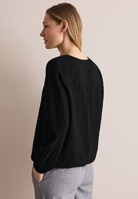 Zwarte longsleeve top met verticale ribbelstructuur, ronde halslijn en een relaxte pasvorm. De achterkant heeft een yoke-naaddetail.