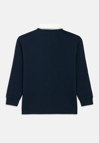 Temno modra majica polo z dolgimi rokavi in belim ovratnikom. Ima rebraste manšete in klasičen kroj. Enobarvna, brez vidnih vzorcev ali poudarkov.