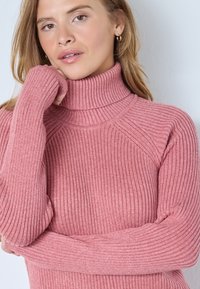 Rosa ribbad polotröja med långa ärmar, som har en åtsittande passform och texturerat mönster. Mjuk material med en mysig look.