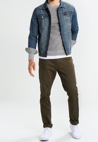 Giacca di jeans blu scuro con bottoni argentati, maglione grigio, t-shirt bianca, pantaloni verde oliva e sneakers bianche. Outfit casual a strati.
