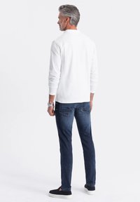 Bílá košile s dlouhým rukávem, slim fit, s manžetami, spárovaná s tmavě modrými džíny a černými nazouvacími teniskami s bílou podrážkou.