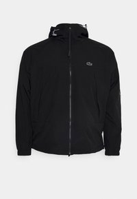 Svart lättviktsjacka med dragkedja, dragsko i huvan, sidofickor och subtil logotyp på övre vänstra bröstet. Slät tygkvalitet.