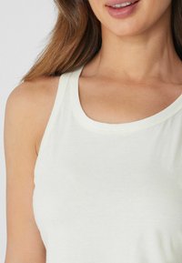 Top sin mangas color marfil claro con escote redondeado y tirantes finos, confeccionado en una tela suave de textura lisa y diseño minimalista.