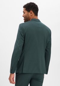 Dunkelgrüner Blazer mit tailliertem Schnitt, mittigem Schlitz und Revers mit Kerbe. Aus strukturiertem Stoff gefertigt, mit Dreiknopf-Manschetten.