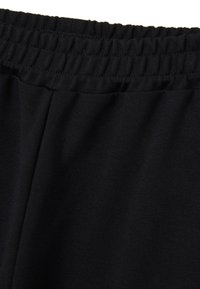 Pantalons de sport noirs avec une taille élastique, en tissu extensible et à texture lisse, conçus pour le confort et la facilité de mouvement.