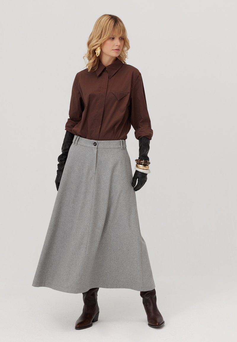 Brązowa koszula z kieszenią, szara spódnica w kształcie dzwonu z detalami w postaci guzików, czarne rękawiczki i brązowe botki za kostkę; gładkie tekstury i neutralne kolory.