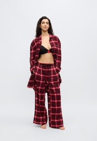 Σετ πιτζάμες φανέλας με κόκκινο και μαύρο καρό σε άνετη εφαρμογή, που περιλαμβάνει πουκάμισο με κουμπιά και παντελόνι με κορδόνι. Μαύρο σουτιέν από κάτω.