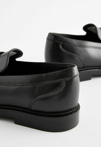 Chaussures en cuir noir avec une finition lisse, une forme arrondie, des coutures visibles et un léger talon. Présentent un design à rabat sur le côté.