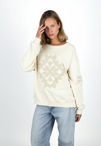 Cremfarbener Pullover mit einem strukturierten Blumenmuster in der Mitte und "HELLO" auf dem linken Ärmel bestickt. Bequeme Passform, Rundhalsausschnitt.