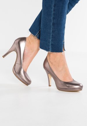 Zapatos de tacón metálico taupe con punta redonda, plataforma y tacón de aguja de 10 cm, combinados con jeans de mezclilla oscuros con dobladillo deshilachado.