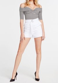 Top de rayas blanco y negro con hombros descubiertos y detalle fruncido, combinado con pantalones cortos blancos de tiro alto que presentan un cinturón y un acabado suave. Tacones negros.