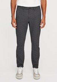 Pantalones grises, ajustados, con una textura suave, corte entallado y una franja lateral en contraste, combinados con zapatillas claras.