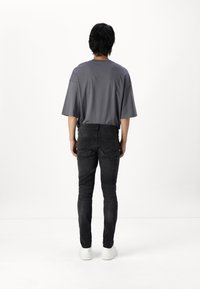 Camiseta gris de gran tamaño, jeans ajustados negros y zapatillas blancas. Diseño minimalista con tela suave y líneas sencillas.