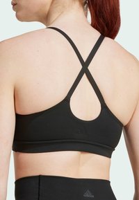 Sujetador deportivo negro con un diseño de espalda redonda y tirantes entrelazados. Textura suave con una marca sutil en el borde inferior.