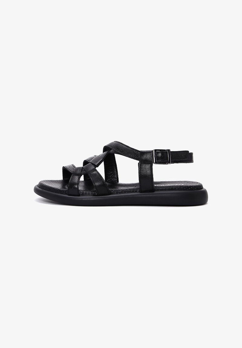 Black leather sandals feature crisscross straps, an adjustable buckle, and a flat rubber sole with a textured insole for grip.