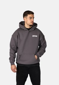 Felpa grigia con cappuccio, dotata di tasca frontale e testo "CRYSTAL" in bianco. Caratterizzata da una vestibilità comoda e una texture morbida, adatta per abbigliamento casual.